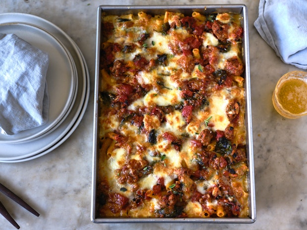 baked ziti being served on a marble table with drinks and plates