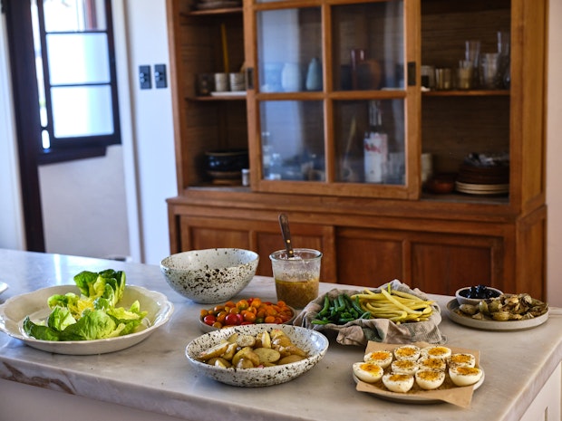 ingredients for a Nicoise arranged on a kitchen island including hard-boiled eggs, green beans, potatoes, olives, lettuces