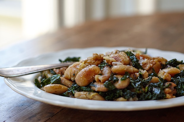 pan-fried beans with kale on a white plate served on a wood table