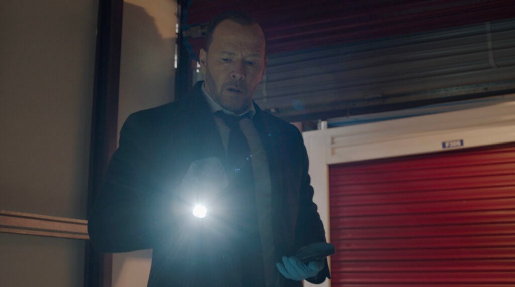 Danny searching a warehouse with a flashlight on Blue Bloods Season 14 Episode 13