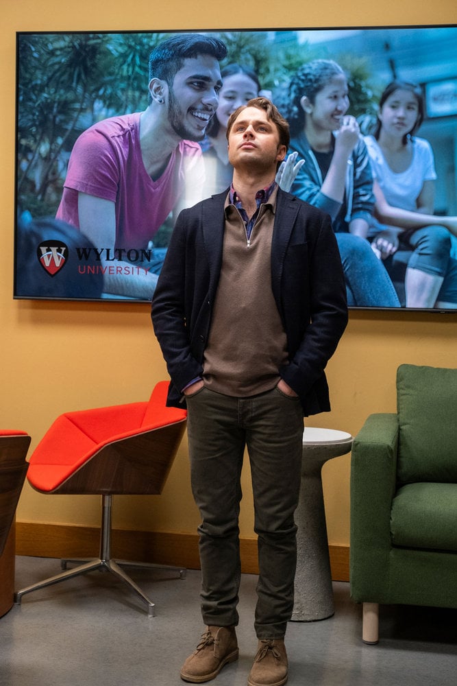 A man standing with his head tilted back in front of a large landscape poster advertising a college