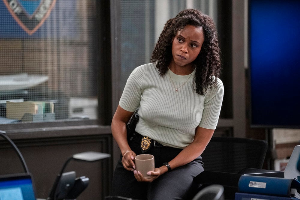 Curry sitting on the edge of her desk with a coffee cup on Law & Order: SVU Season 26 Episode 2