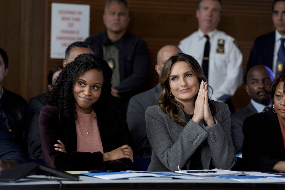 BEnson sitting at a meeting next to Curry, smiling and pressing her hands together on Law & Order: SVU Season 26 Episode 3