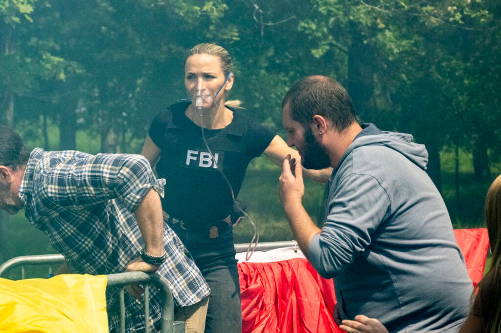 Nina wearing a gas mask and helping two bearded men escape a dangerous situation on FBI: Most Wanted Season 6 Episode 3