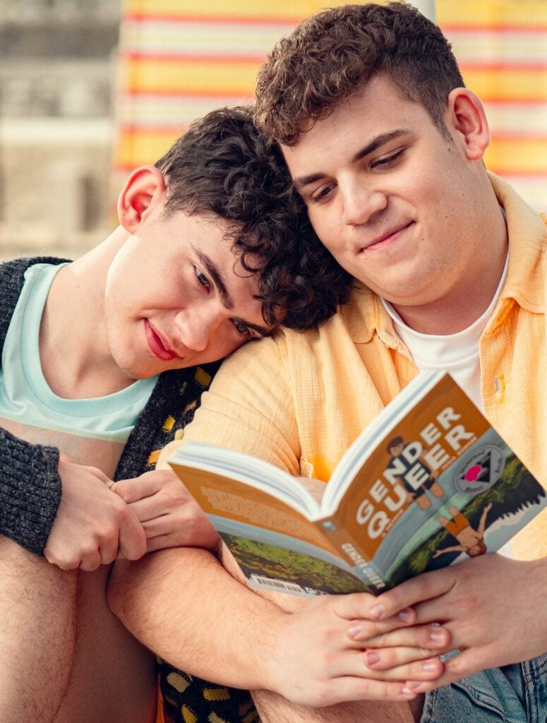 Charlie leans on Isaac while Isaac reads a book called Gender Queer on Heartstopper