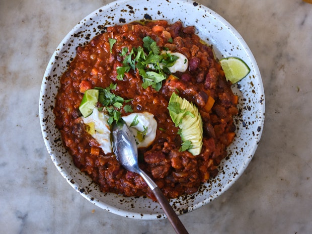 bowl of vegan chili topped with sour cream, lime, cilatnro and avocado