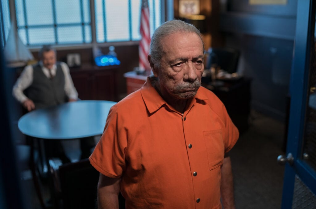 Lorenzo Batista in the prison visiting room, with a blurry Frank at the visitors table behind him, on Blue Bloods Season 14 Episode 18