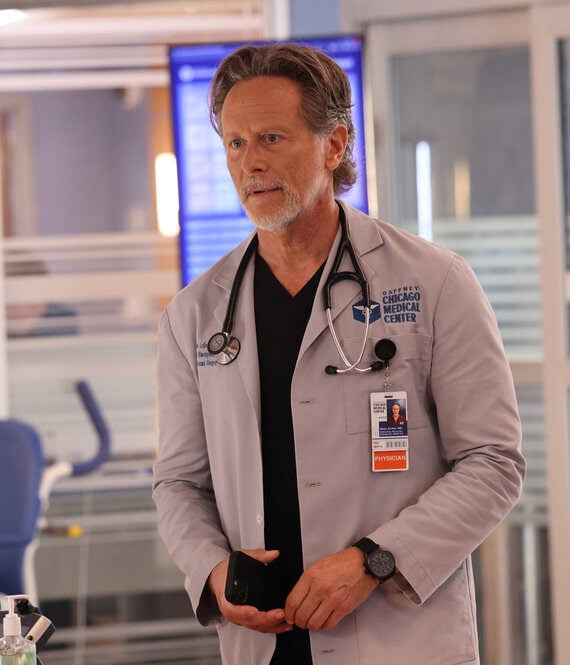 Dr. Archer standing by an empty wheelchair holding a phone on Chicago Med Season 10 Episode 4